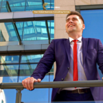 Satisfied business professional in a suit standing on an office balcony and looking across the city skyline, representing international business growth and corporate strategy.